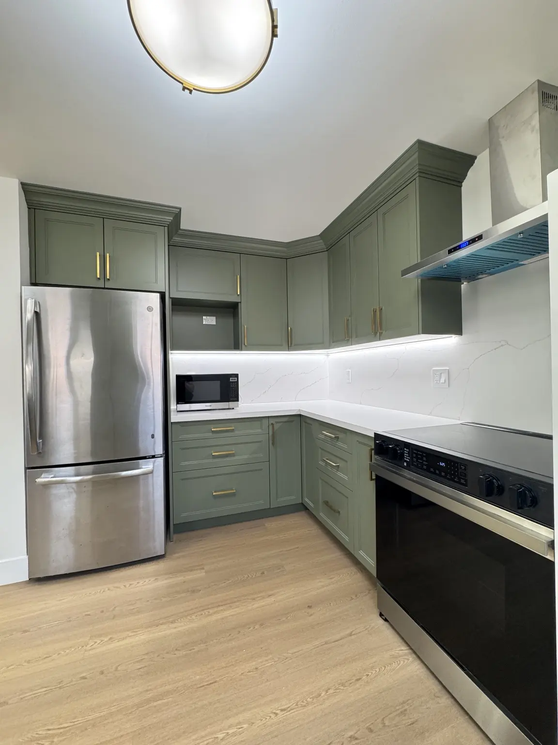 Green kitchen with stainless steel appliances, range and statement exhaust hood