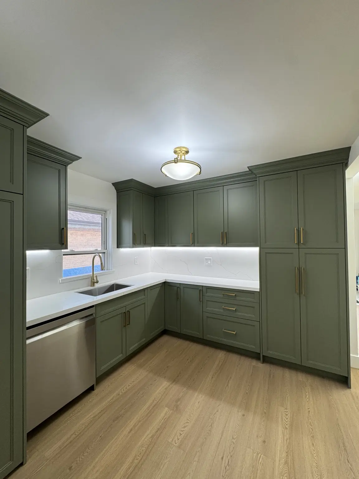 Custom sage kitchen cabinets with brass hardware, quartz counters and integrated lighting