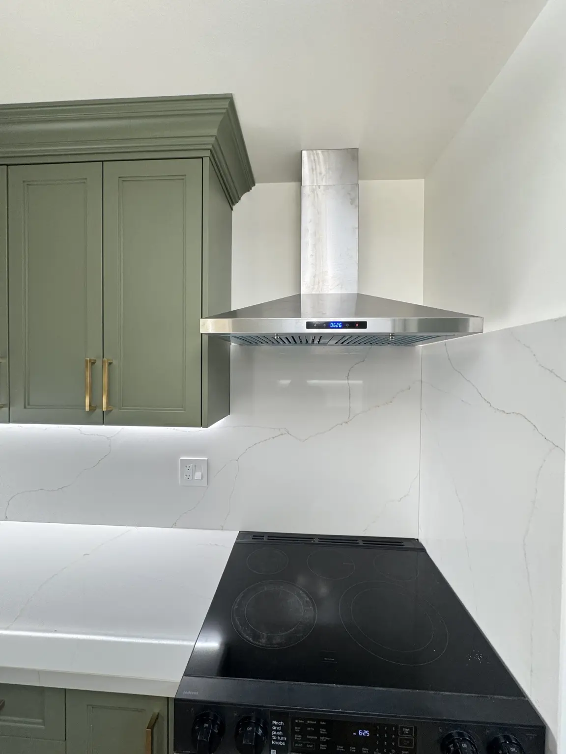 Quartz backsplash surrounding the cooktop and stainless steel range hood