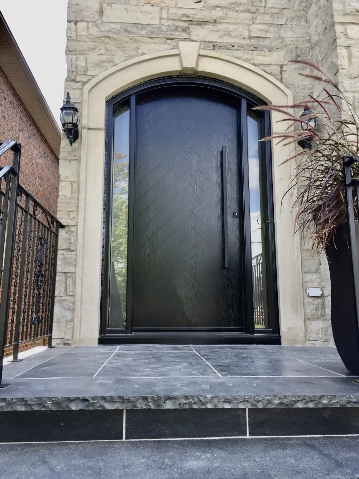 Modern black front entrance door framed by the home’s existing stone façade