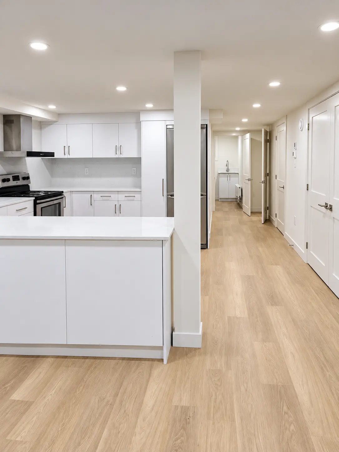 Bright basement kitchen and hallway with white cabinetry and wood-look flooring