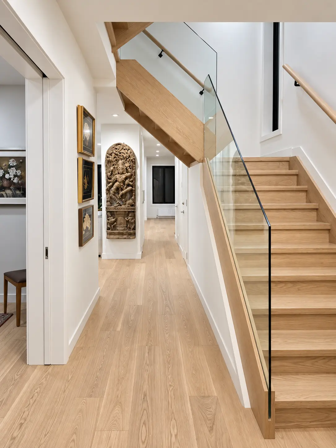 Oak staircase with clear glass railing and matching hallway flooring