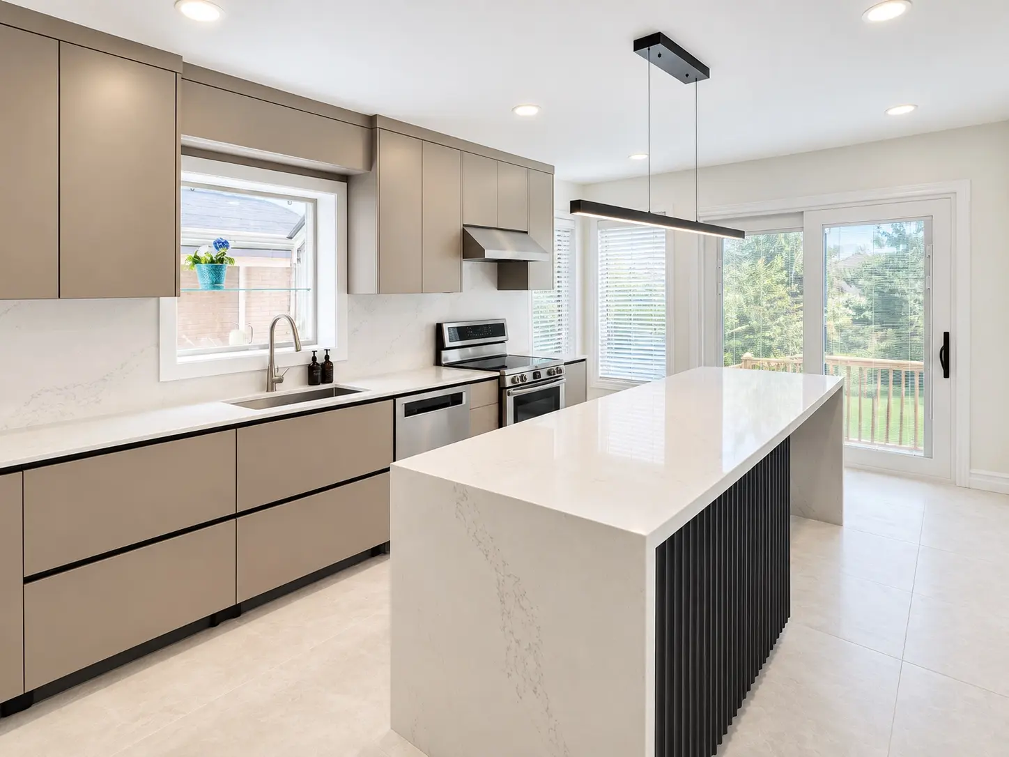 Side view of the modern kitchen showing the long quartz island and open connection to the backyard